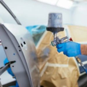 Technician using a spray gun to paint a car door in a repair shop